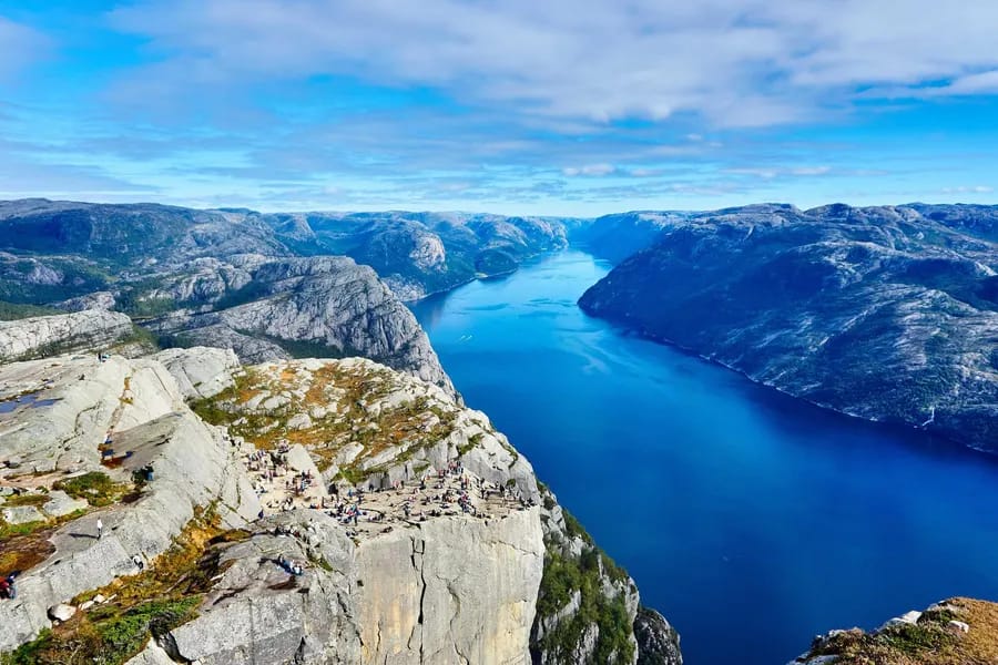A deep blue fjord winding between rocky mountains seen from a high cliff edge.