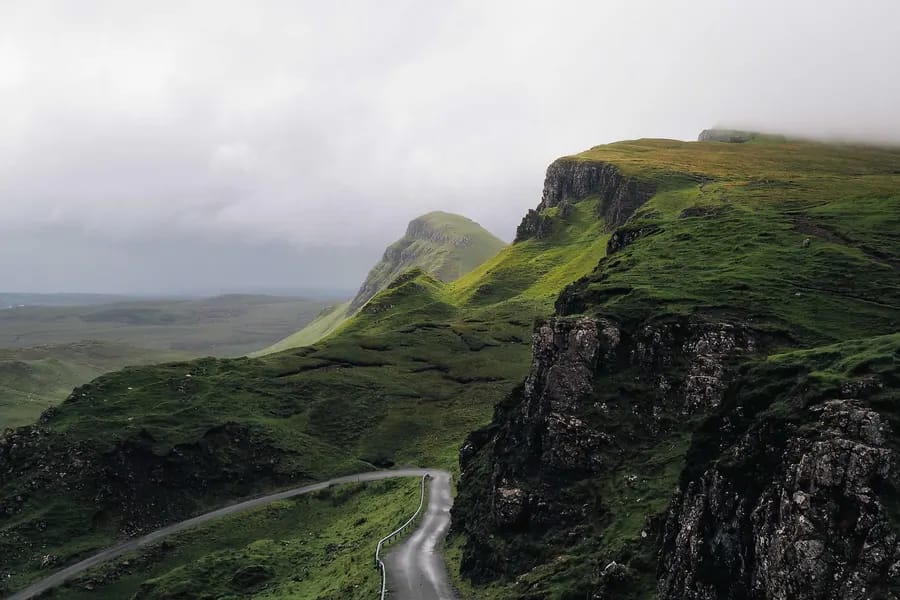 Steep green cliffs and a winding road under a soft grey sky.