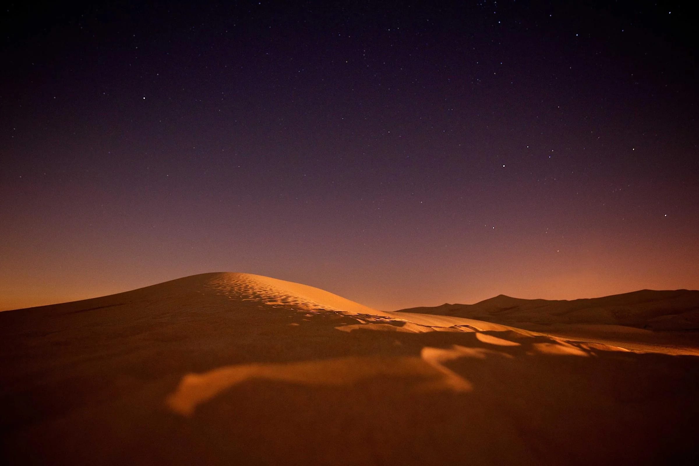 Smooth desert dunes in deep amber tones beneath a dark violet night sky.